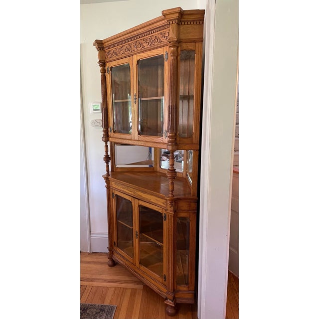 This large vintage corner cabinet showcases beautifully designed oak features and beveled glass panes and mirrors...