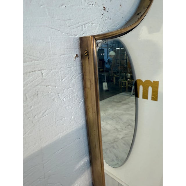 Italian wall mirror from the 1950s distinguished by a graceful shield-shaped silhouette framed in brass.His curvilinear...