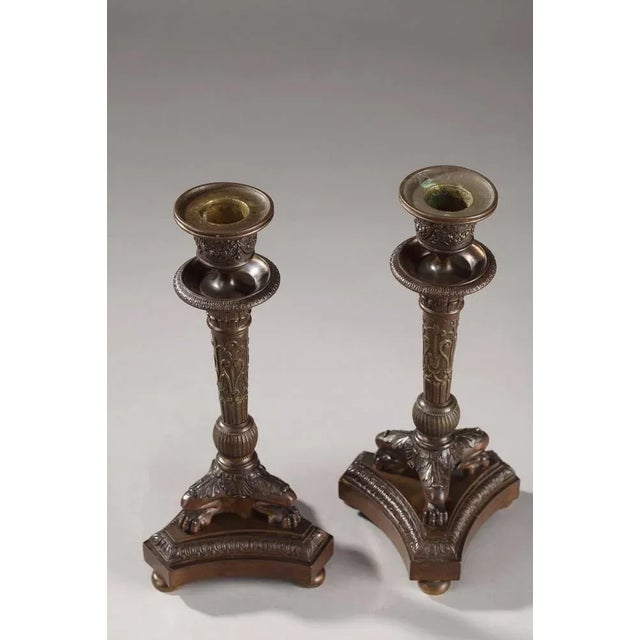 Pair of small, patinated bronze candlesticks resting on three lion's feet that are embellished with palmettes and acanthus...