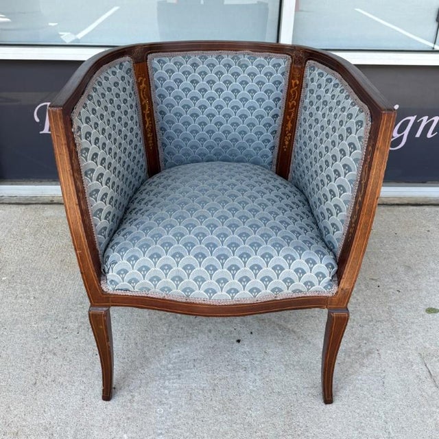 This elegant barrel-back chair features a warm wood frame accented with delicate inlay, gently curved sides, and slender...