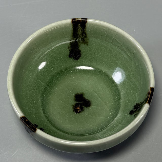 This antique Chinese Longquan celadon bowl features attractive dark splashed spots over the soft green glaze, with natural...