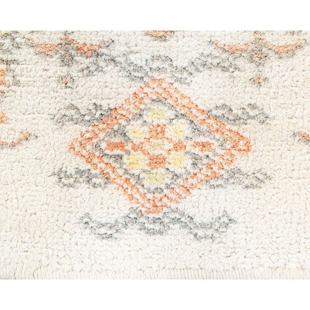 This vintage Cotton Agra rug features a captivating, intricate design composed of symmetrical floral patterns set against...