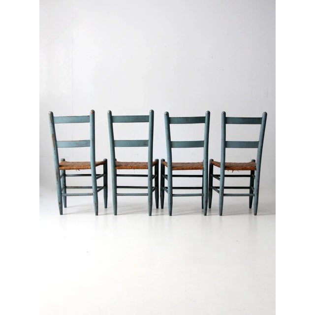 A set of four antique wooden chairs with woven seats. Each chair features a soft eggshell blue painted finish,...