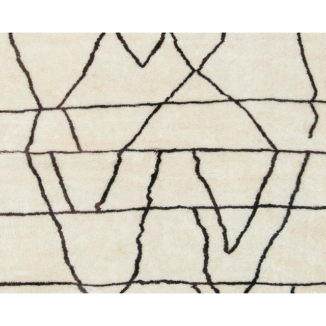 Artistic hand-knotted wool rug with a smooth, Ivory base and abstract Espresso lines inspired by traditional Berber...