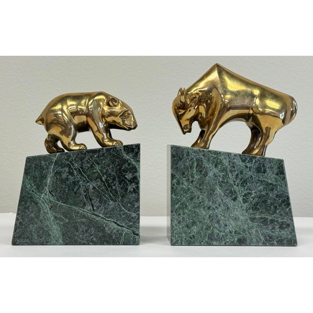 Vintage bookends featuring brass bull and bear of the stock market and Wall Street atop heavy green marble bases. Age...