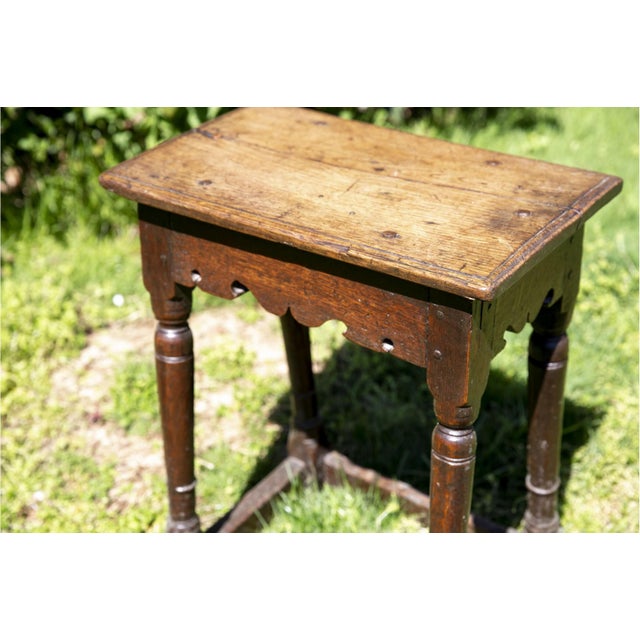 An antique English oak joint stool with a rich dark brown patina and visible grain, rectangular solid wood top, scalloped...