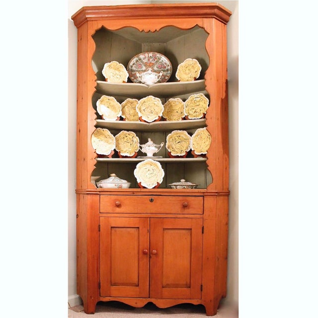 A charming ca. 1830’s two piece corner cupboard with an artfully scalloped edge open front top cabinet resting on a lower...