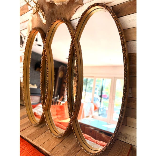 A glamorous Hollywood Regency statement mirror featuring three interlocking vertical oval panels set in a heavily ornate...