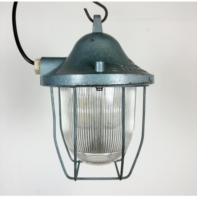Blue industrial lamp made by Polam Gdansk in Poland during the 1960s. It features a cast aluminium body, an iron cage and...