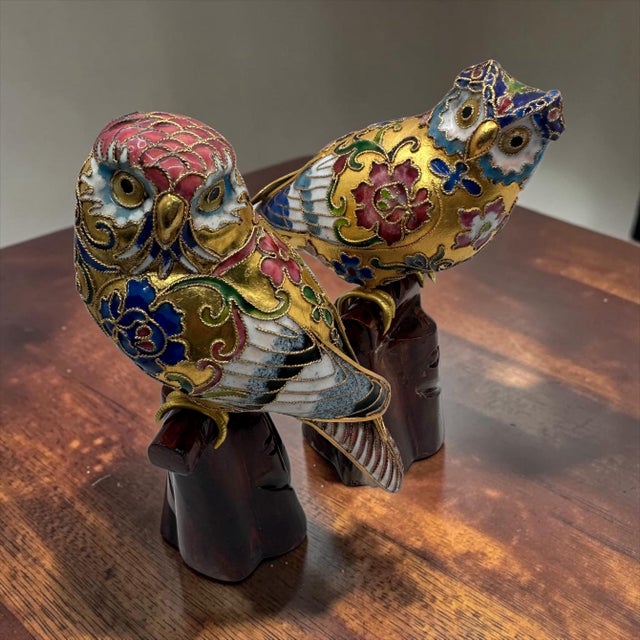 A pair of traditional Chinese cloisonné owl figurines featuring intricate enamel work and gold leaf details perched on...