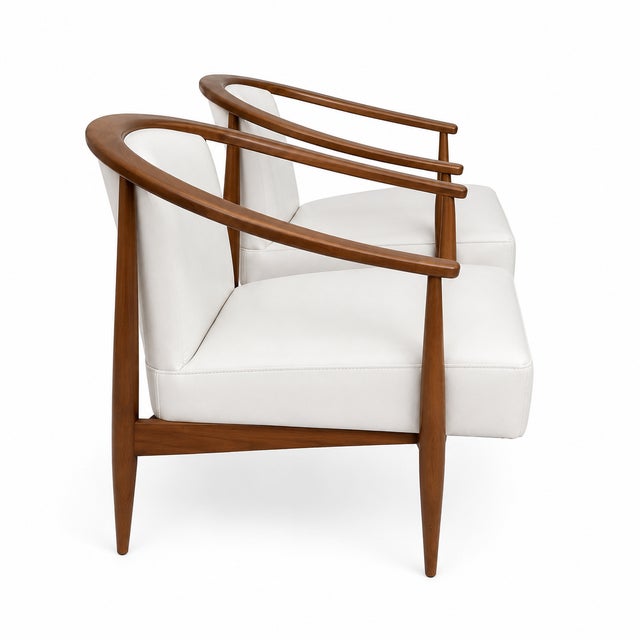 Modern mid century lounge chairs done in a cream leather upholstery. The chairs have a walnut finish. The chairs are circa...