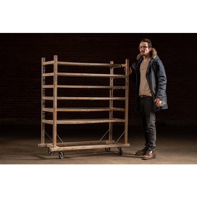 Tall rolling drying rack constructed with a painted wood frame reinforced by steel bracing and mounted on four swivel...