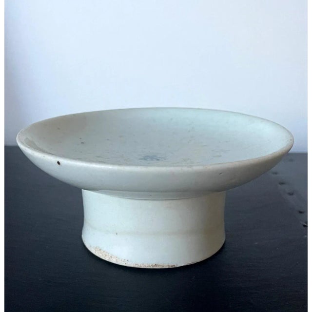 A small ceramic stemmed dish with high cylindrical foot in white glaze with a cobalt blue underglaze inscription in the...