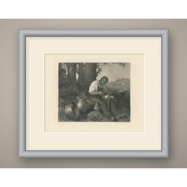 An elderly tinker sits on the ground at the edge of a wood, absorbed in his work. Bent forward in a white shirt with...