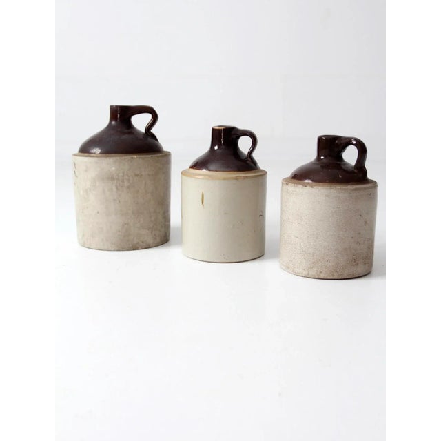 This is a collection of three antique stoneware crock jugs. These antique utilitarian pieces are beautiful statements in...