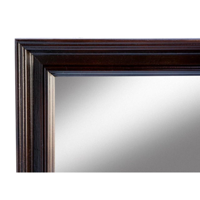 A wood framed mirror featuring a rich brown stain applied over its original painted finish. The technique creates a...