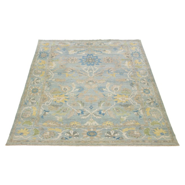 This hand-knotted Sultanabad wool rug has a light blue background with multicolored all-over designs. This rug measures...