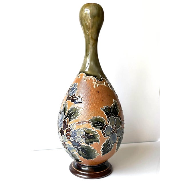 Exquisitely designed stoneware vase with tubelined blue-green glazed floral design on textured tan ground. Bulbous form...