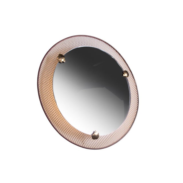 Elegant round wall mirror with backlighting on a perforated metal frame with brass finishes. The mirror, positioned in the...