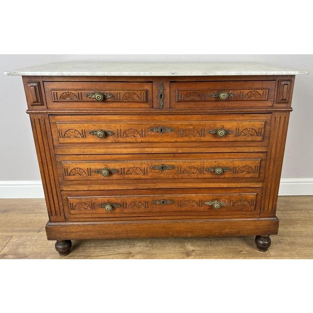 An elegant Antique French chest of drawers in walnut, featuring a white marble top, five drawers and beautifully detailed...