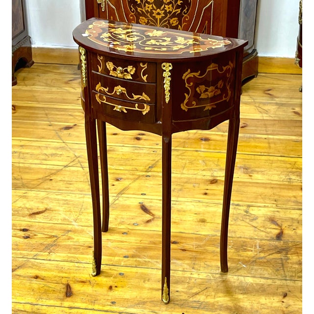 This elegant French-style demilune side table features a rich dark wood finish enhanced by intricate floral marquetry and...
