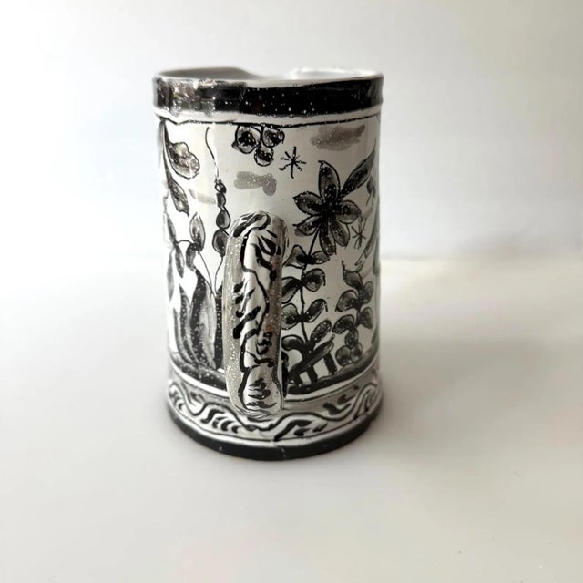 Flowers, foliage, figures and a castle decorate this charming black and white handled pitcher made in Portugal. Perfect to...