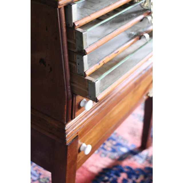 Antique spool drawer with glass front thin drawers and brass tab handles. On legs with 2 larger drawers with white ceramic...