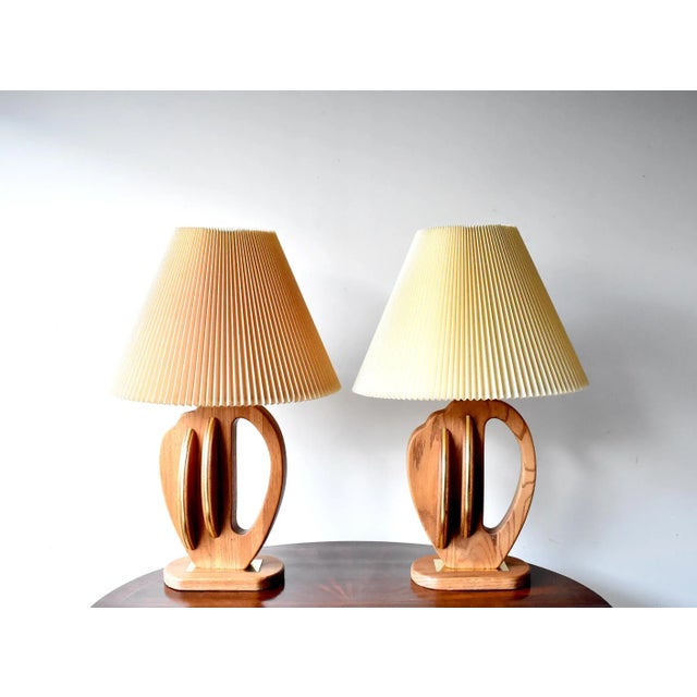 A pair of mid-century modern sculptural table lamps in oak wood and brass, c. 1950s. Original pleated shades, one a little...