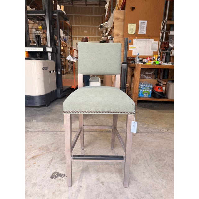 Contemporary counter stool featuring clean lines and a tailored silhouette upholstered in a soft green woven fabric. The...