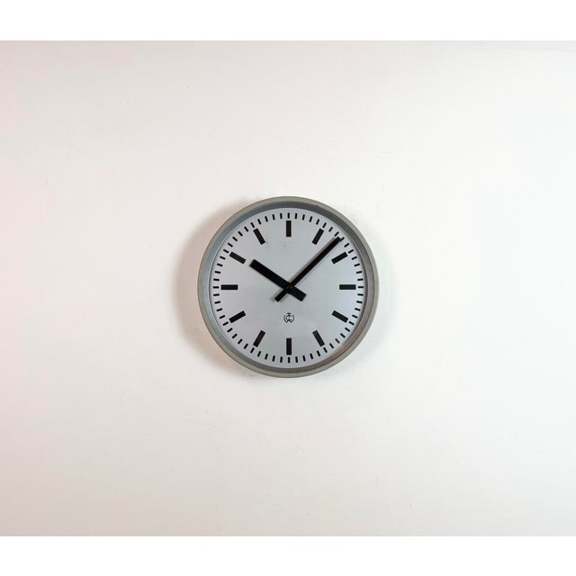 TCW post office wall clock was made in Netherlands during the 1960s. It features a grey iron frame, a metal dial, an...