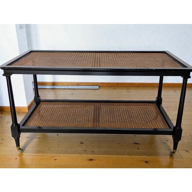 A two-tier, British Colonial style rectangular coffee table with a black lacquered wood frame, woven hand-caned inset...