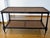 A two-tier, British Colonial style rectangular coffee table with a black lacquered wood frame, woven hand-caned inset...
