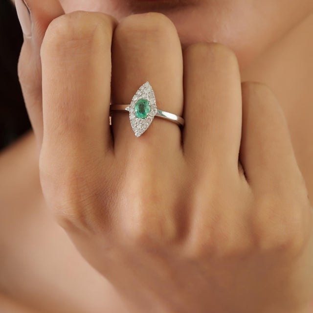 The Diamond-Studded Regal Emerald Engagement Ring features an elegant marquise-shaped halo surrounding a vibrant oval...