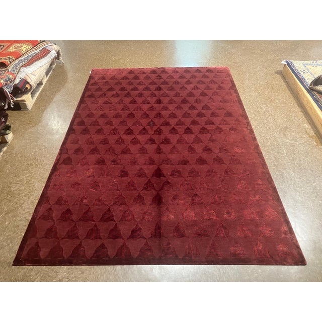 Hand-loomed Nepal wool rug featuring a deep red field with an allover repeating geometric motif in a subtle tonal...