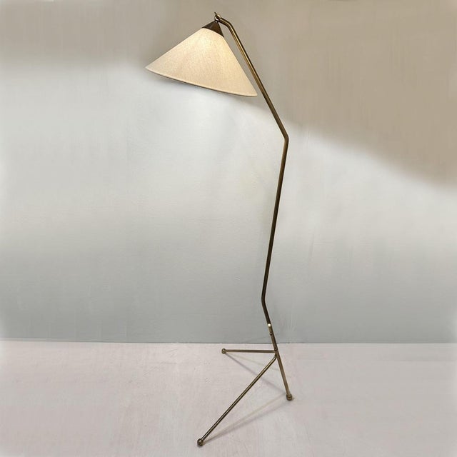 Elegant Italian floor lamp dating from the 1950's, featuring a slender brass frame and tripod legs. The tapered shade has...