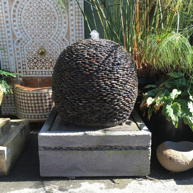 Beautiful modern fountain crafted of rounded river stone pebbles framed to a sphere that sits on top of a matching base /...