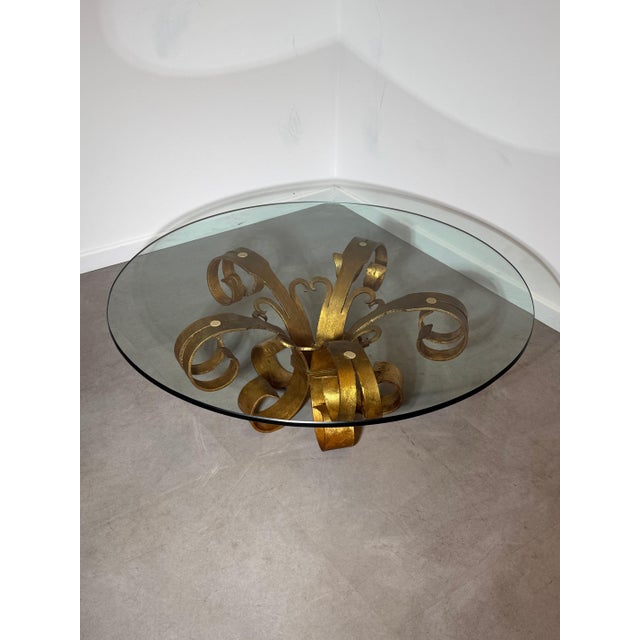 An elegant vintage coffee table featuring a sculptural gilt iron base with beautifully hand-forged scrollwork and a...