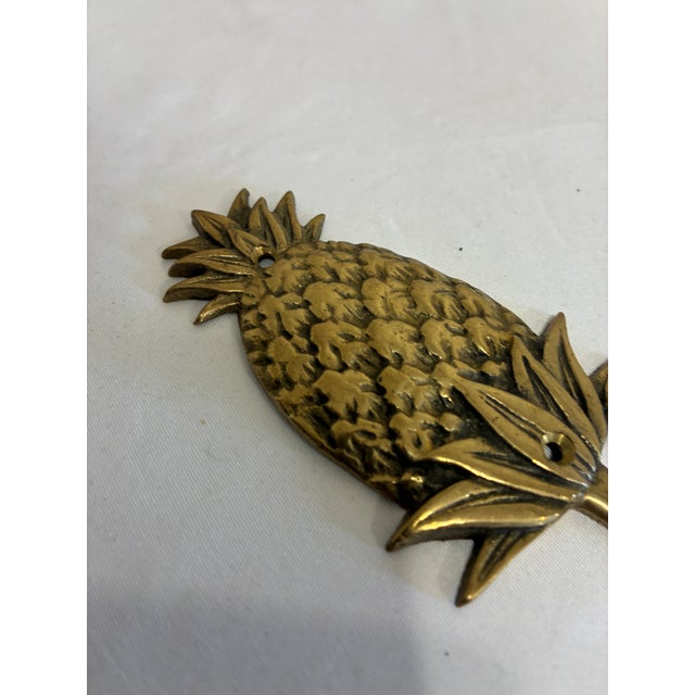 A charming vintage solid brass hook in the shape of a pineapple, with a richly textured fruit, crisp pointed leaves, and a...