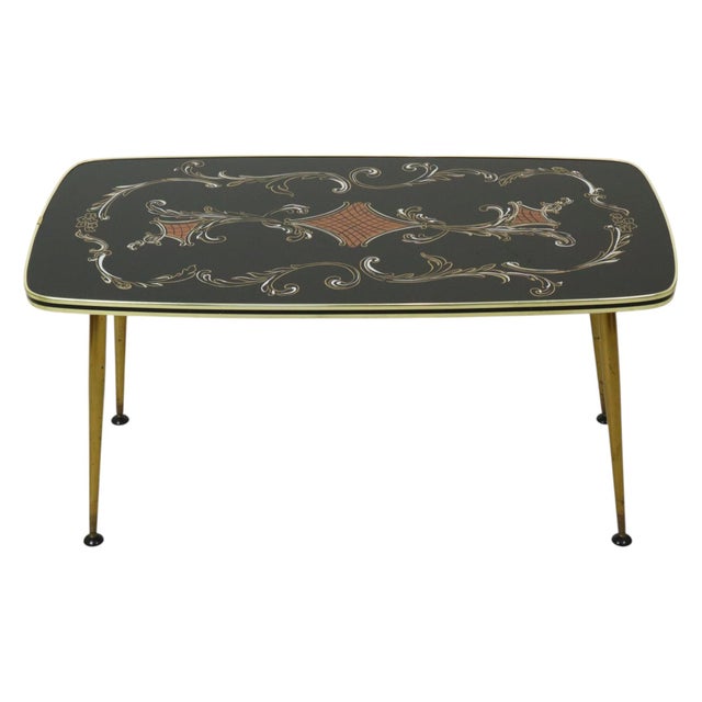Vintage coffee table with a glass top; the black surface features a floral acanthus motif and a gold band with a central...