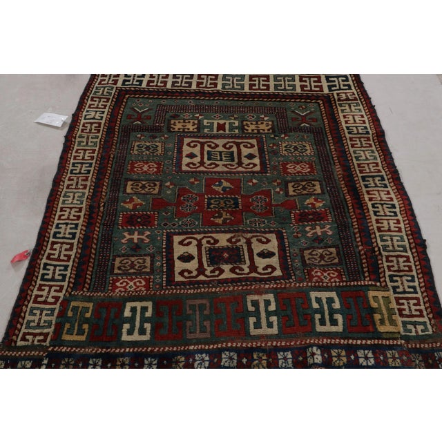 This Antique tribal kazak rug, handmade in wool, in Teal, with red and blue all over geometric patterns showcases the...