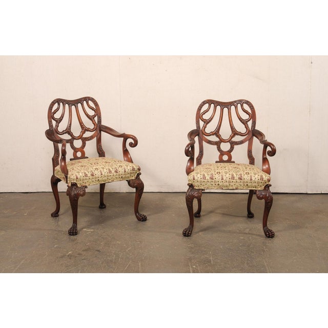 An English pair of wooden armchairs, with richly carved decorative details and elegant proportions, from the early 20th...