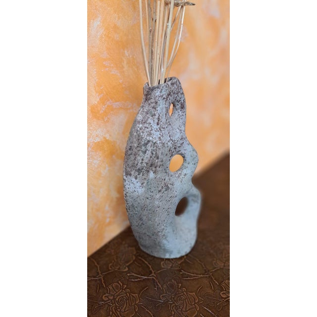 Handmade vase in a biomorphic and brutalist style, characterized by its circular perforations and a mottled texture that...