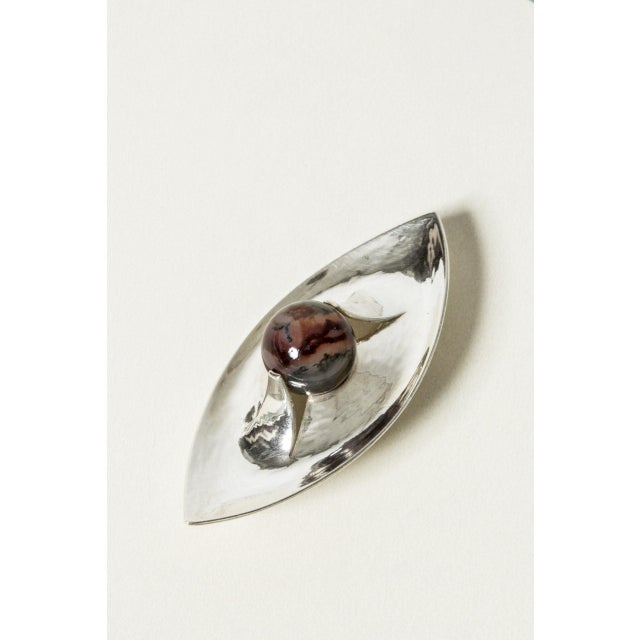 Beautiful silver brooch by Elis Kauppi, in a boat form with a hammered surface that creates a rippling effect. A round...