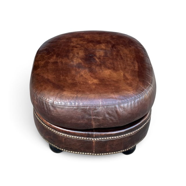 This vintage oval ottoman is upholstered in rich brown leather with a naturally aged patina that gives it warmth and...