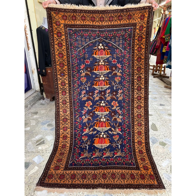 This exquisite hand-knotted wool area rug showcases a traditional Baluchi prayer rug layout featuring a unique Tree of...