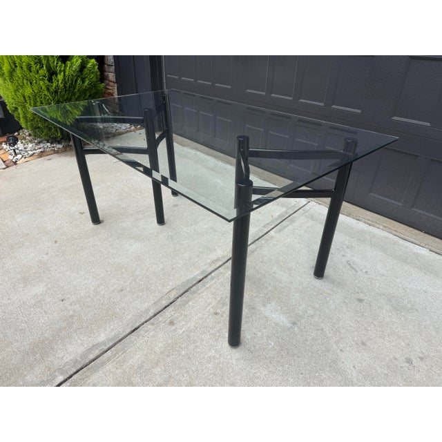 Sleek vintage postmodern dining table featuring a thick rectangular glass top paired with a sculptural black metal tubular...