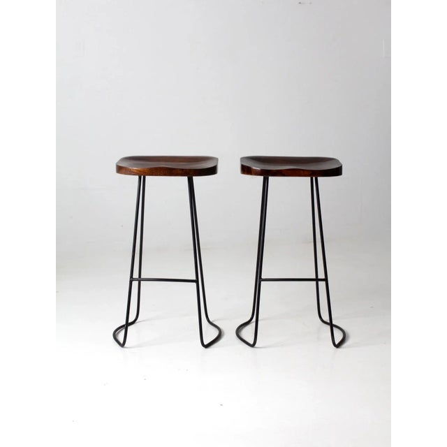 This is a pair of mid 20th century stools. Dynamic metal legs with curving design and wood saddle seats make these a...