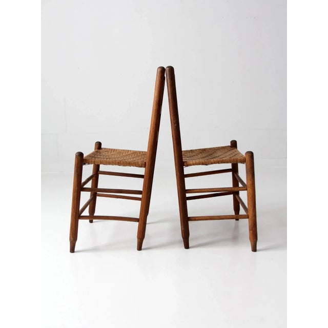 A pair of antique splint-weave seat chairs with a rustic, timeworn character. The wooden chairs feature classic ladder...