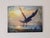 This artwork captures a bird in mid-flight against a vibrant sunset, blending warm hues of orange and yellow with cool...