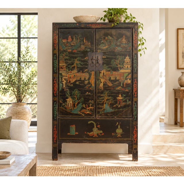 A tall Chinese armoire in black lacquer, painted across both doors with a landscape of pagodas, arched bridges, willows...